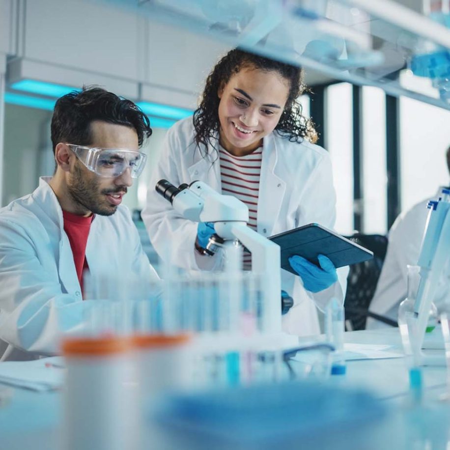 Portrait-of-Latin-and-Black-Young-Scientists-Using-Microscope-Digital-Tablet-Doing-Sample-Analysis-Talking-aspect-ratio-1600-975