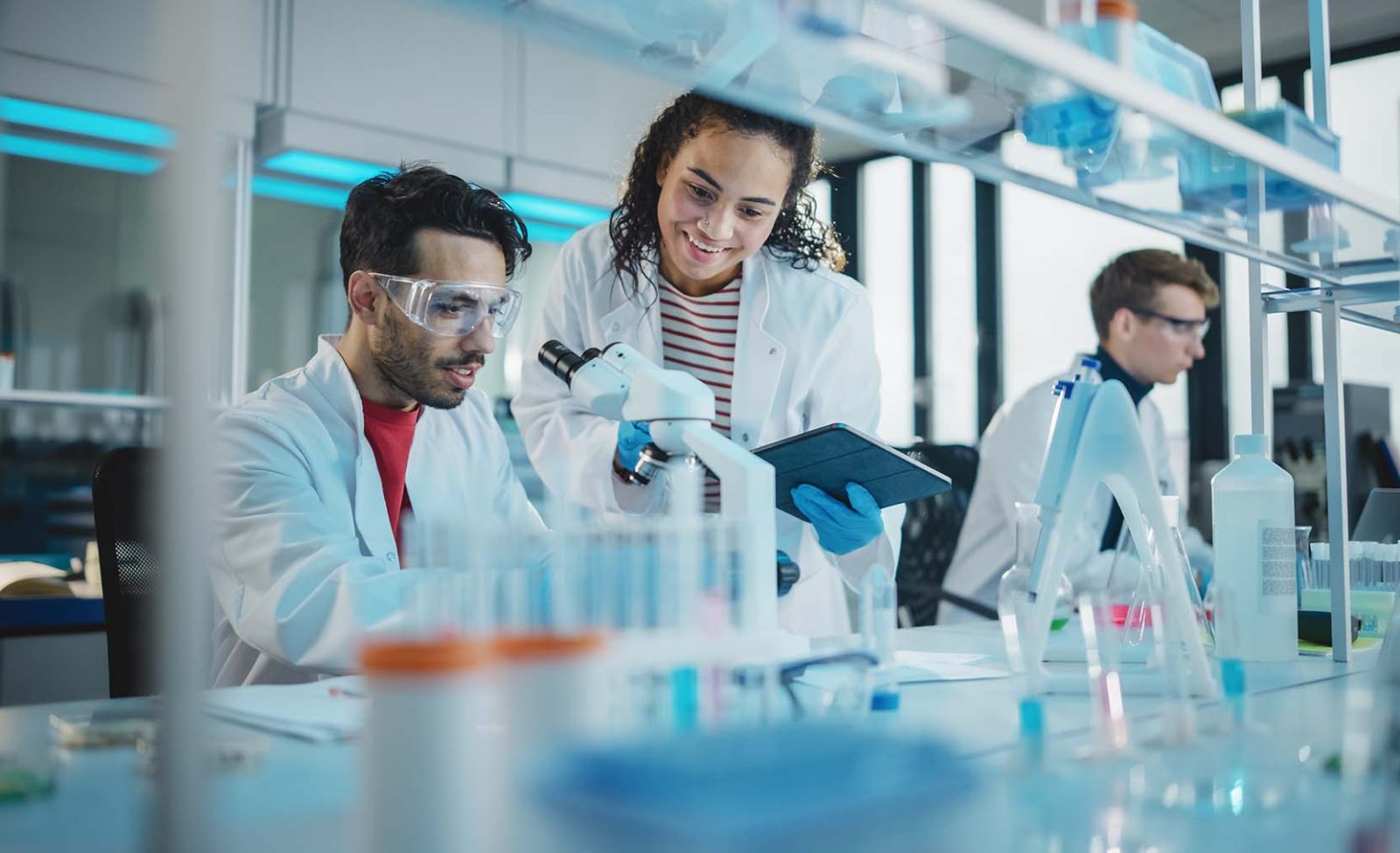 Portrait-of-Latin-and-Black-Young-Scientists-Using-Microscope-Digital-Tablet-Doing-Sample-Analysis-Talking-aspect-ratio-1600-975