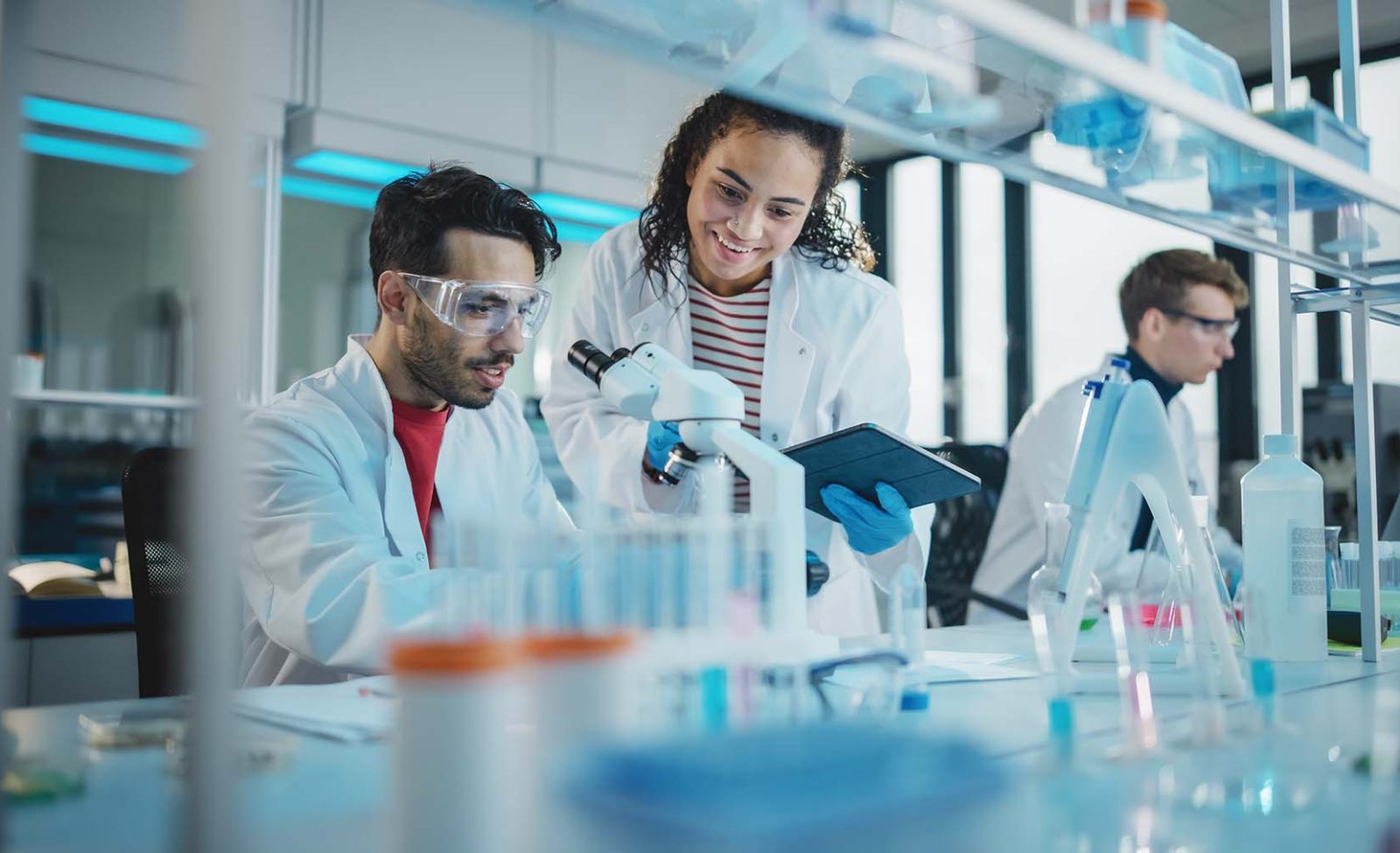 Portrait-of-Latin-and-Black-Young-Scientists-Using-Microscope-Digital-Tablet-Doing-Sample-Analysis-Talking-aspect-ratio-1600-975